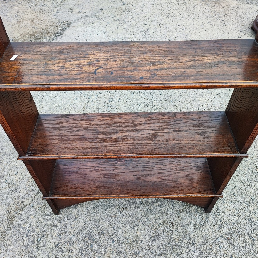 A low three-tier open oak bookcase featuring shaped side uprights and an arched apron base. View V