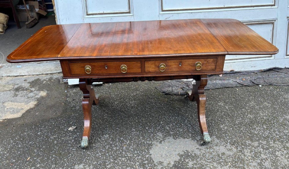 A Regency mahogany sofa table featuring two hinged drop leaves, two frieze drawers with brass ring handles, and splayed legs ending in brass paw castors. View III