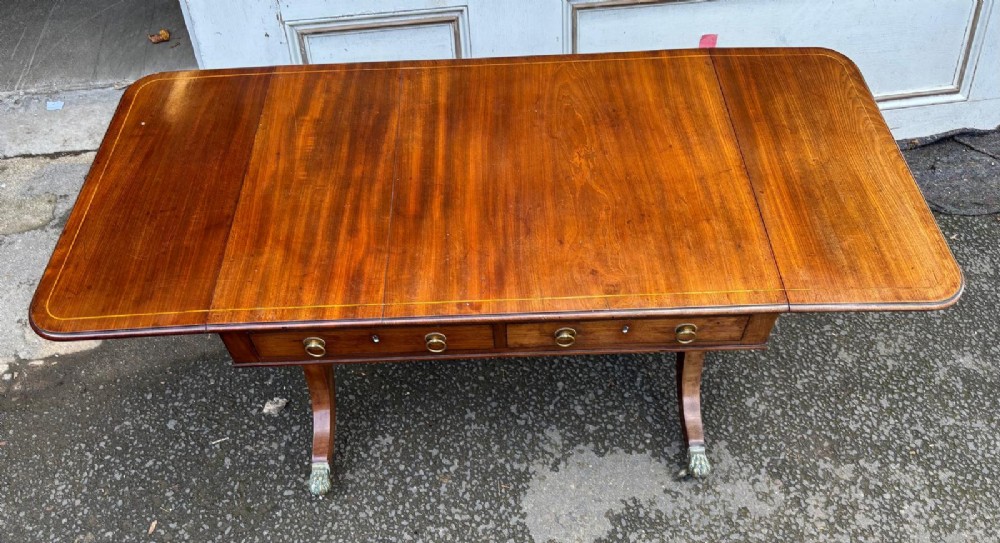 A Regency mahogany sofa table featuring two hinged drop leaves, two frieze drawers with brass ring handles, and splayed legs ending in brass paw castors. View IV