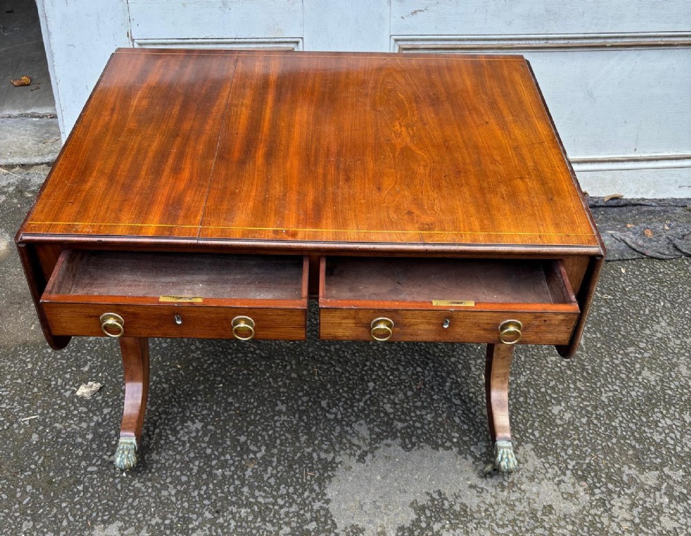 A Regency mahogany sofa table featuring two hinged drop leaves, two frieze drawers with brass ring handles, and splayed legs ending in brass paw castors. View V