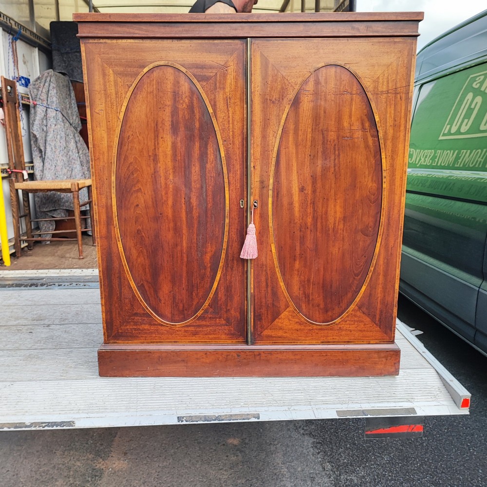 An antique dark mahogany two-door storage cupboard with decorative oval inlay panels set on a solid plinth base. View II