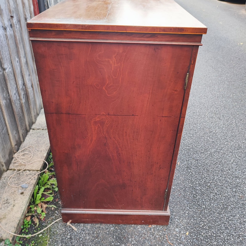 An antique dark mahogany two-door storage cupboard with decorative oval inlay panels set on a solid plinth base. View IV