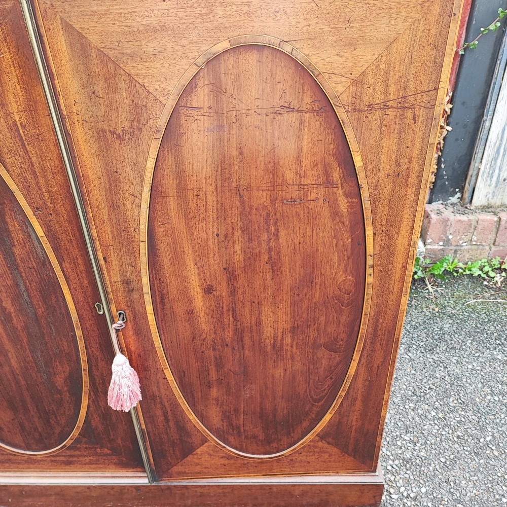 An antique dark mahogany two-door storage cupboard with decorative oval inlay panels set on a solid plinth base. View VII