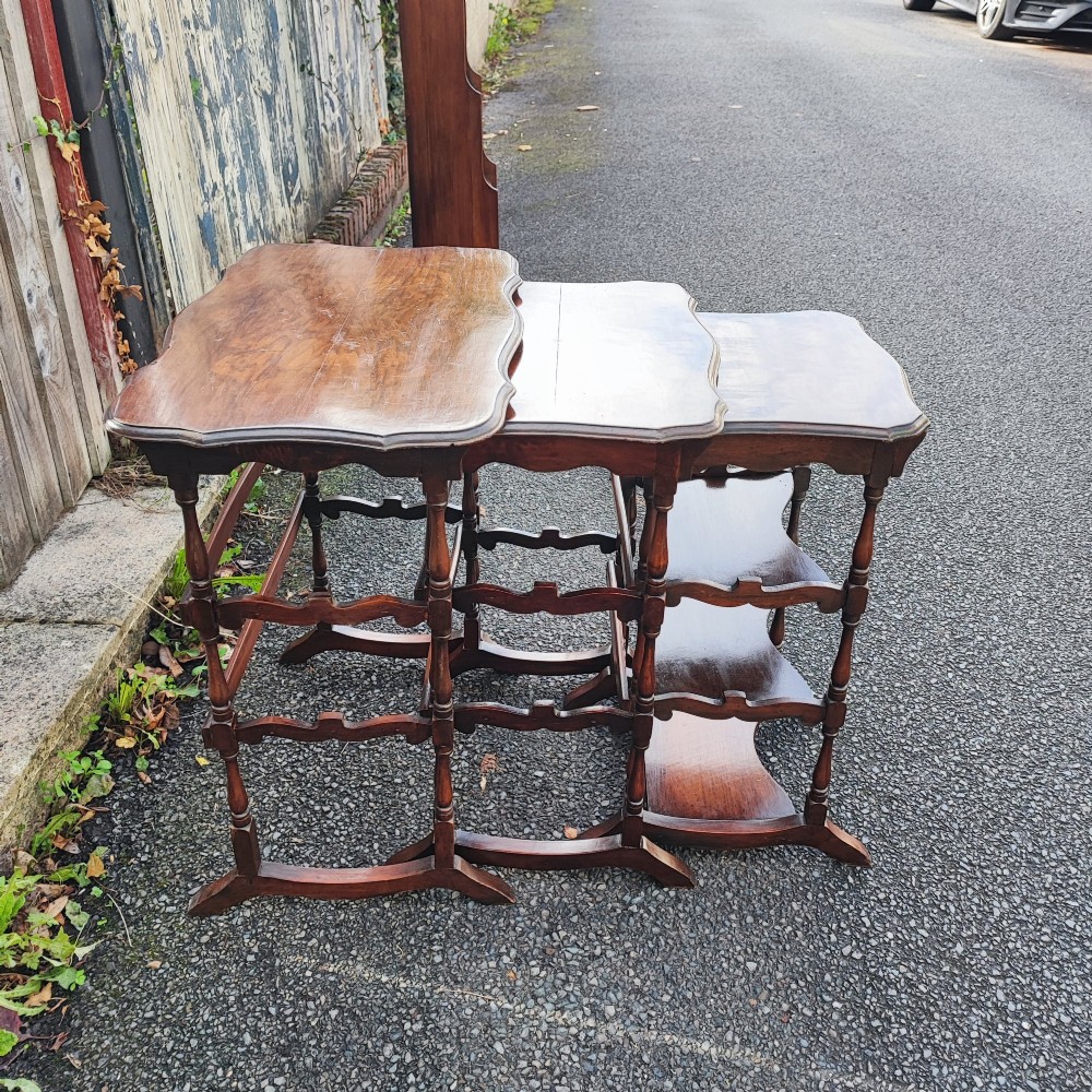A set of three antique walnut nesting tables with serpentine edges and turned legs stacked together. View II