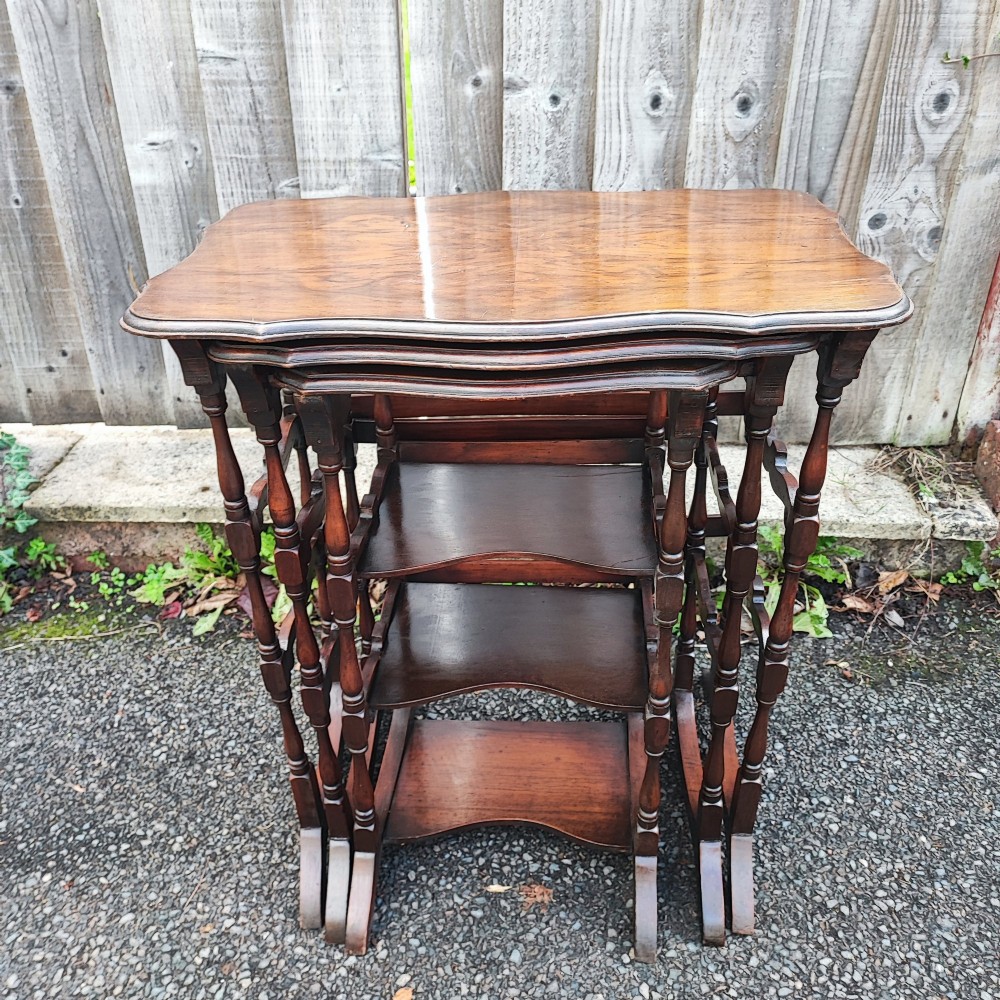 A set of three antique walnut nesting tables with serpentine edges and turned legs stacked together. View IV