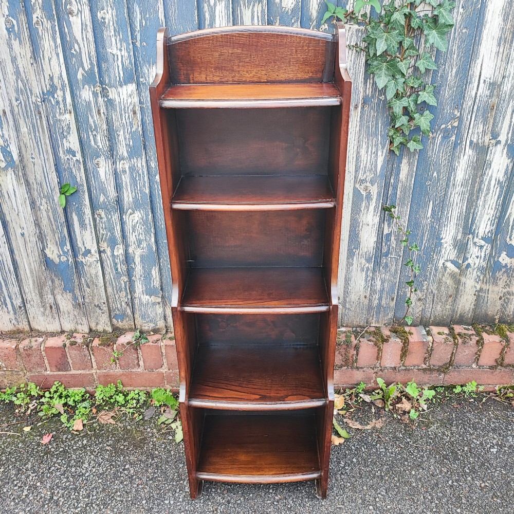 A tall, narrow dark oak open bookcase with five tiered shelves and a curved top gallery.