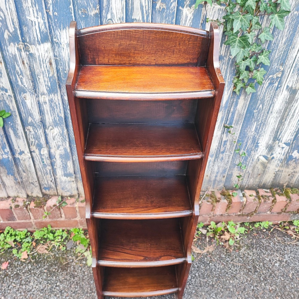 A tall, narrow dark oak open bookcase with five tiered shelves and a curved top gallery. View IV