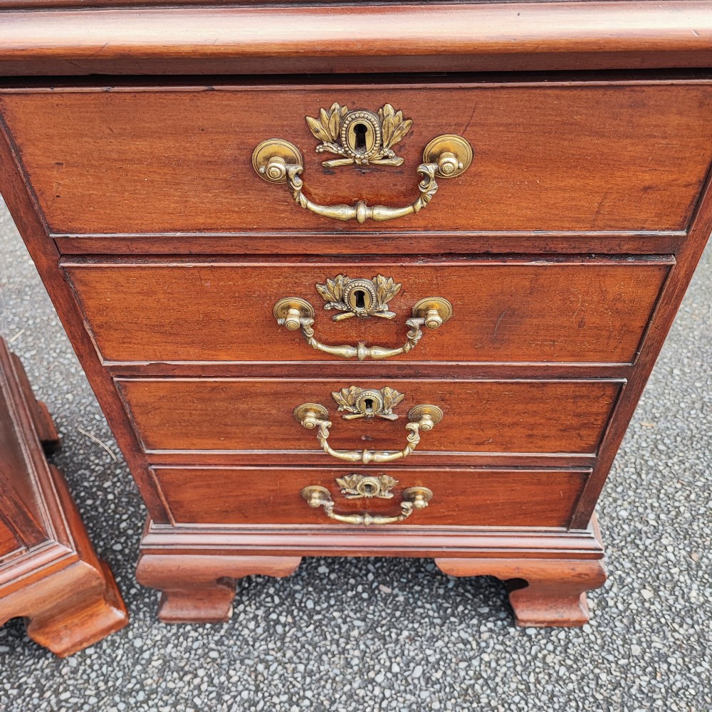 A pair of small warm brown mahogany chests of drawers featuring inset leather tops, four drawers with brass swan-neck handles, and shaped bracket feet. View II
