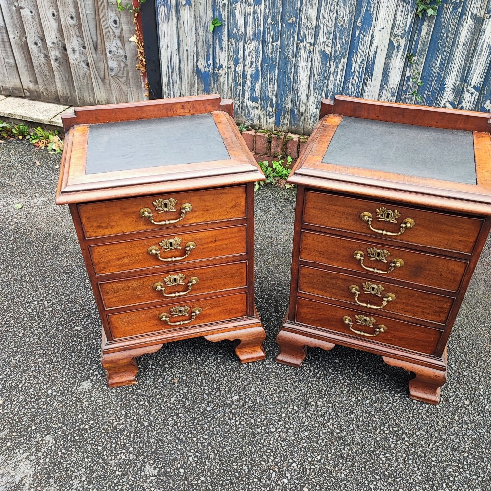 A pair of small warm brown mahogany chests of drawers featuring inset leather tops, four drawers with brass swan-neck handles, and shaped bracket feet. View X