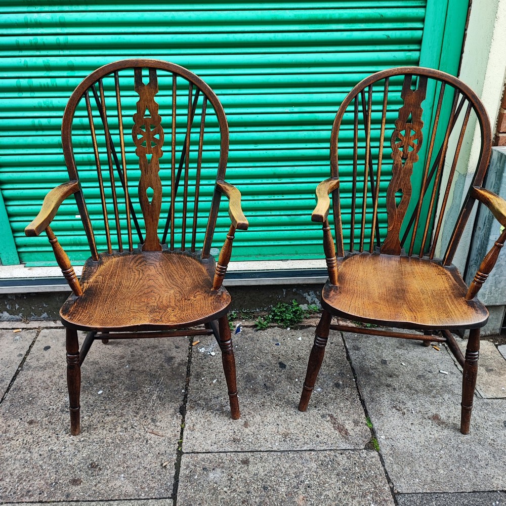 A pair of antique wooden Windsor armchairs featuring pierced wheelback splats, curved arms, shaped saddle seats, and turned legs.