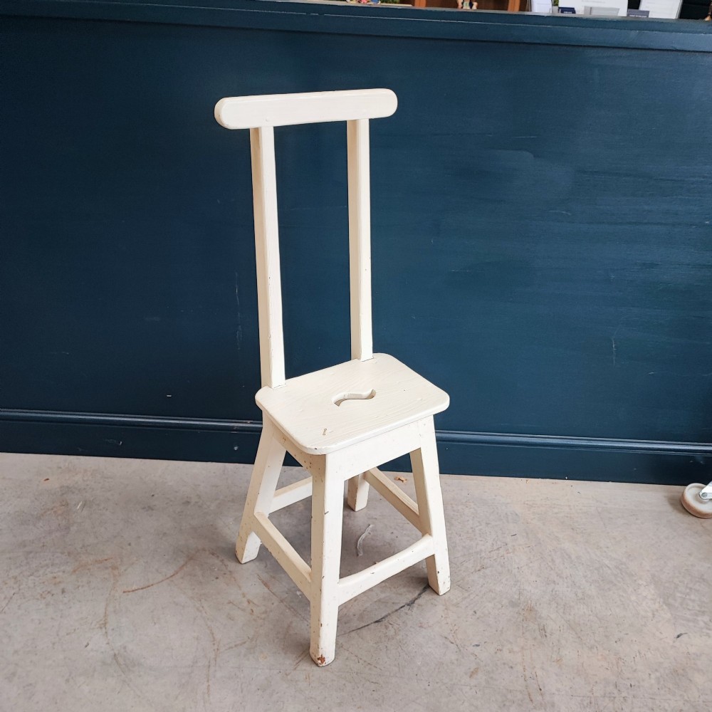 An off-white painted wooden step stool featuring a tall vertical back handle, splayed square legs, and a seat with a central carved handhole.