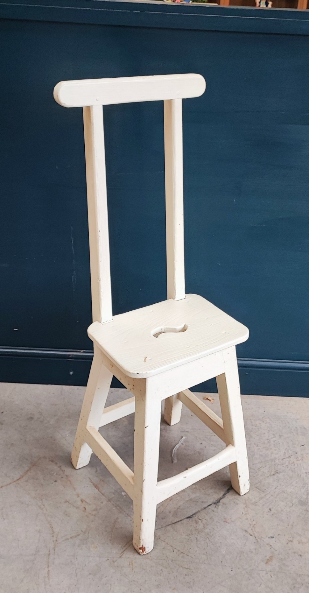 An off-white painted wooden step stool featuring a tall vertical back handle, splayed square legs, and a seat with a central carved handhole. View II