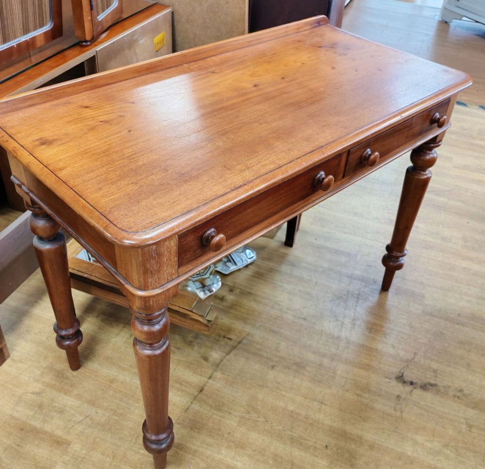A Victorian mahogany writing table featuring a rectangular top with a low raised edge, two frieze drawers with turned wooden knobs, and turned legs.