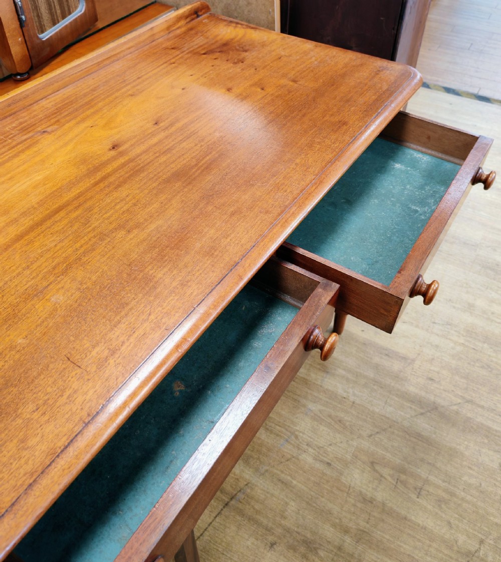 A Victorian mahogany writing table featuring a rectangular top with a low raised edge, two frieze drawers with turned wooden knobs, and turned legs. View II