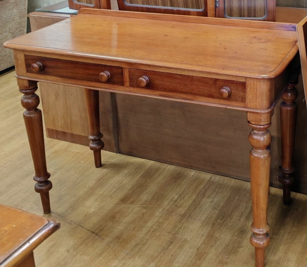 A Victorian mahogany writing table featuring a rectangular top with a low raised edge, two frieze drawers with turned wooden knobs, and turned legs. View V