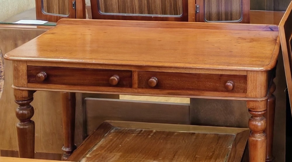 A Victorian mahogany writing table featuring a rectangular top with a low raised edge, two frieze drawers with turned wooden knobs, and turned legs. View VII