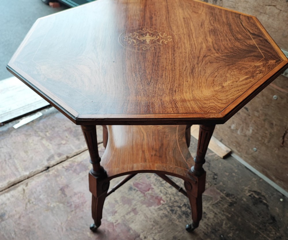 An octagonal Victorian rosewood occasional table with central marquetry inlay, slender turned legs, a lower undertier, and brass castors.