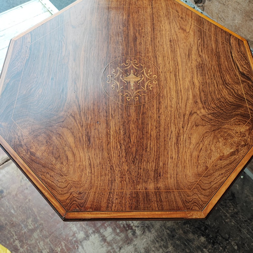 An octagonal Victorian rosewood occasional table with central marquetry inlay, slender turned legs, a lower undertier, and brass castors. View II
