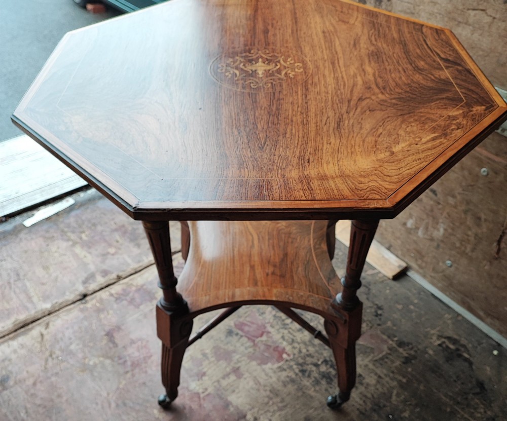 An octagonal Victorian rosewood occasional table with central marquetry inlay, slender turned legs, a lower undertier, and brass castors. View VI