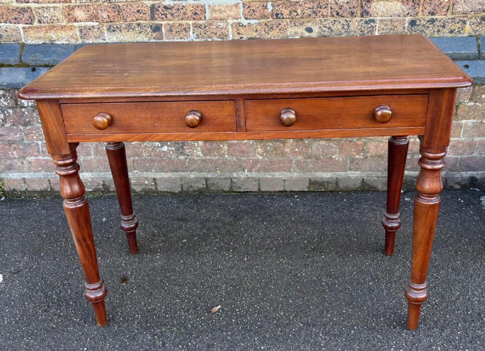 A Victorian mahogany writing table featuring a rectangular top, two front drawers with turned wooden knob handles, and four turned legs.