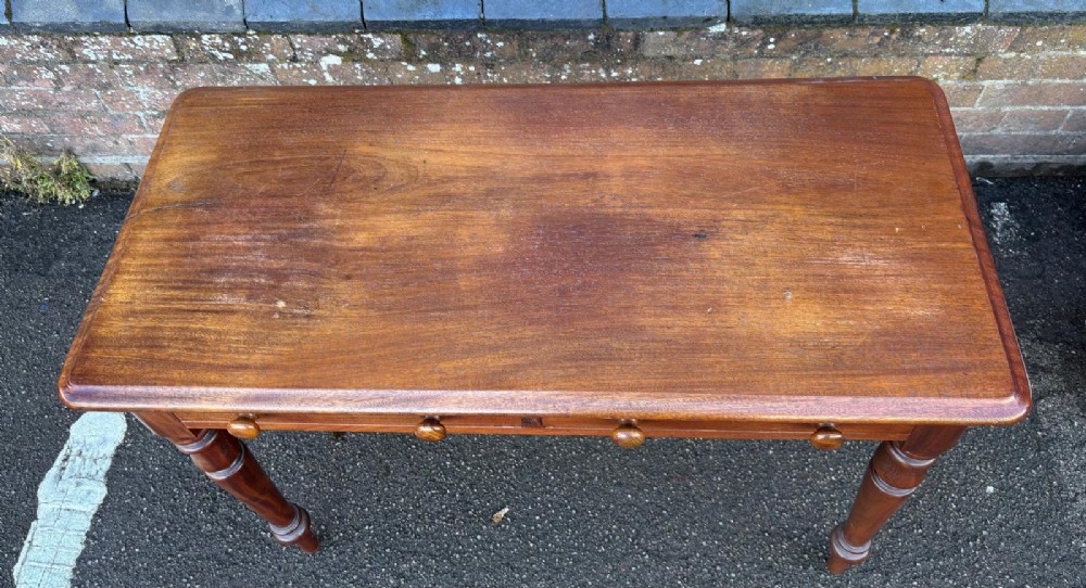 A Victorian mahogany writing table featuring a rectangular top, two front drawers with turned wooden knob handles, and four turned legs. View V