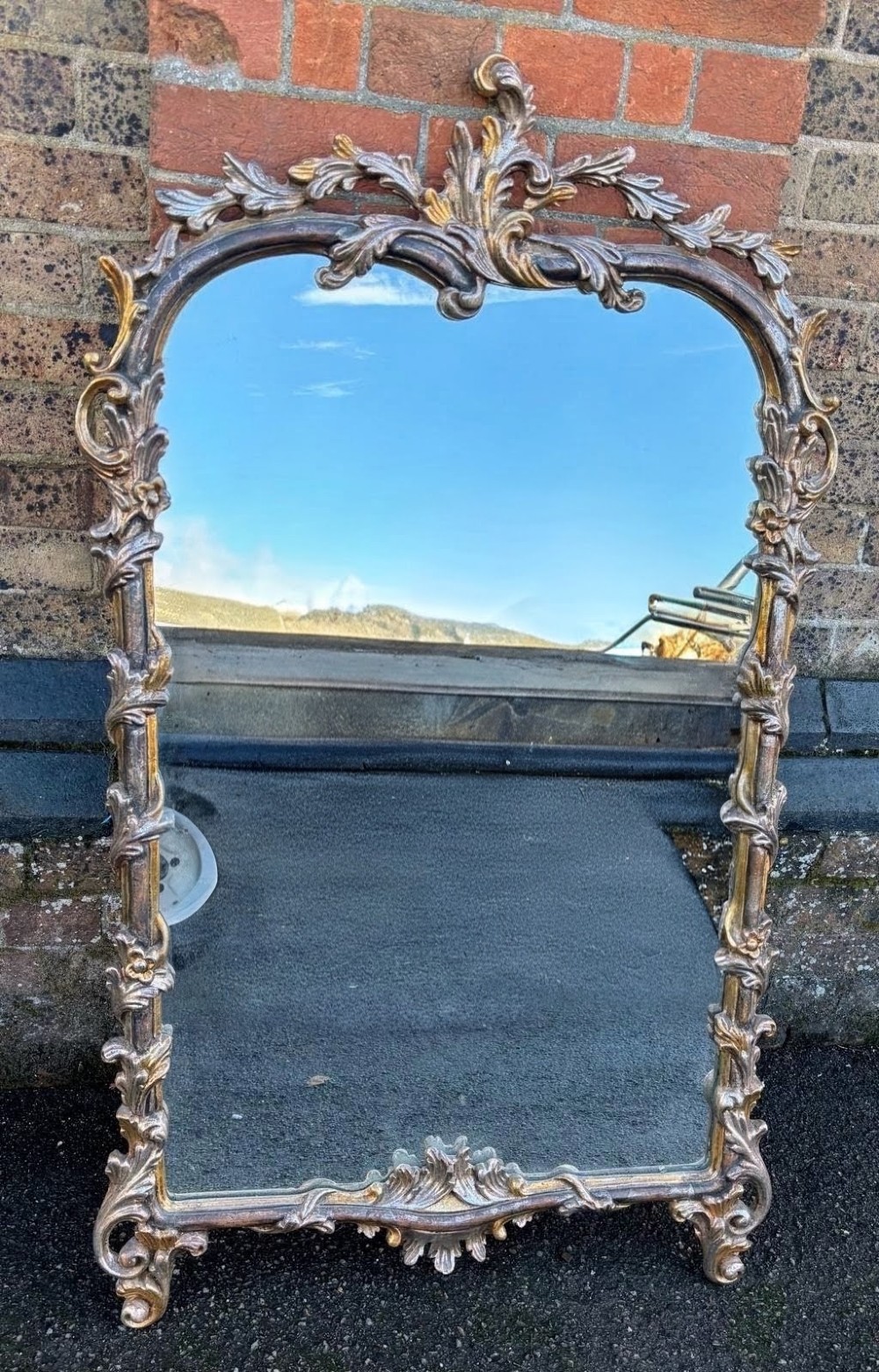 A large 20th-century Italian wall mirror featuring an arched top and an ornate carved wood frame finished in silver and gold leaf with acanthus leaf motifs.