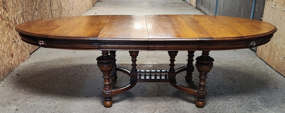 A large Victorian golden oak extending dining table featuring an oval top, carved rope-twist frieze, and elaborate turned legs joined by a central stretcher. View II
