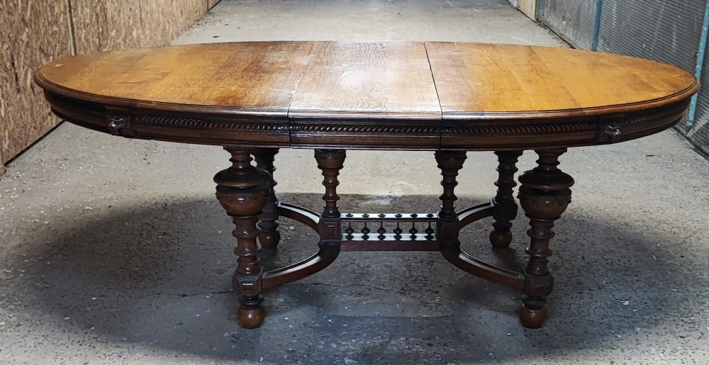 A large Victorian golden oak extending dining table featuring an oval top, carved rope-twist frieze, and elaborate turned legs joined by a central stretcher. View VI