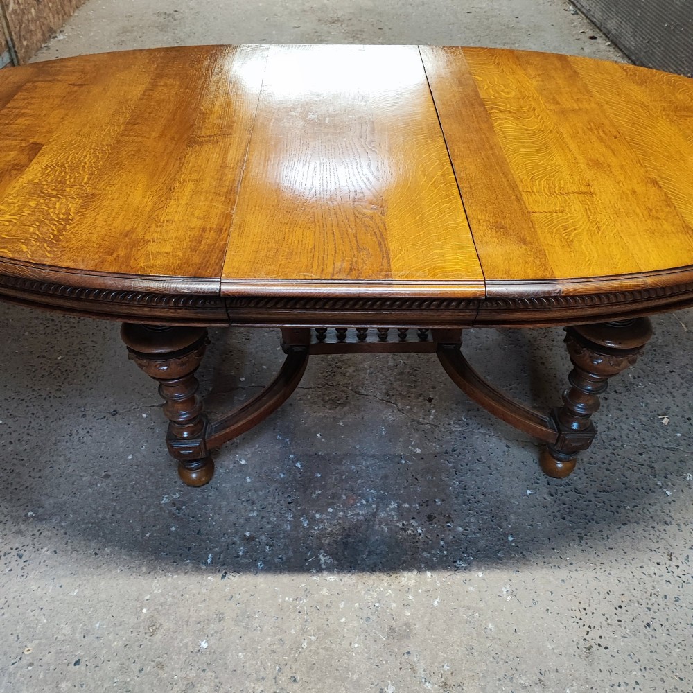 A large Victorian golden oak extending dining table featuring an oval top, carved rope-twist frieze, and elaborate turned legs joined by a central stretcher. View VII