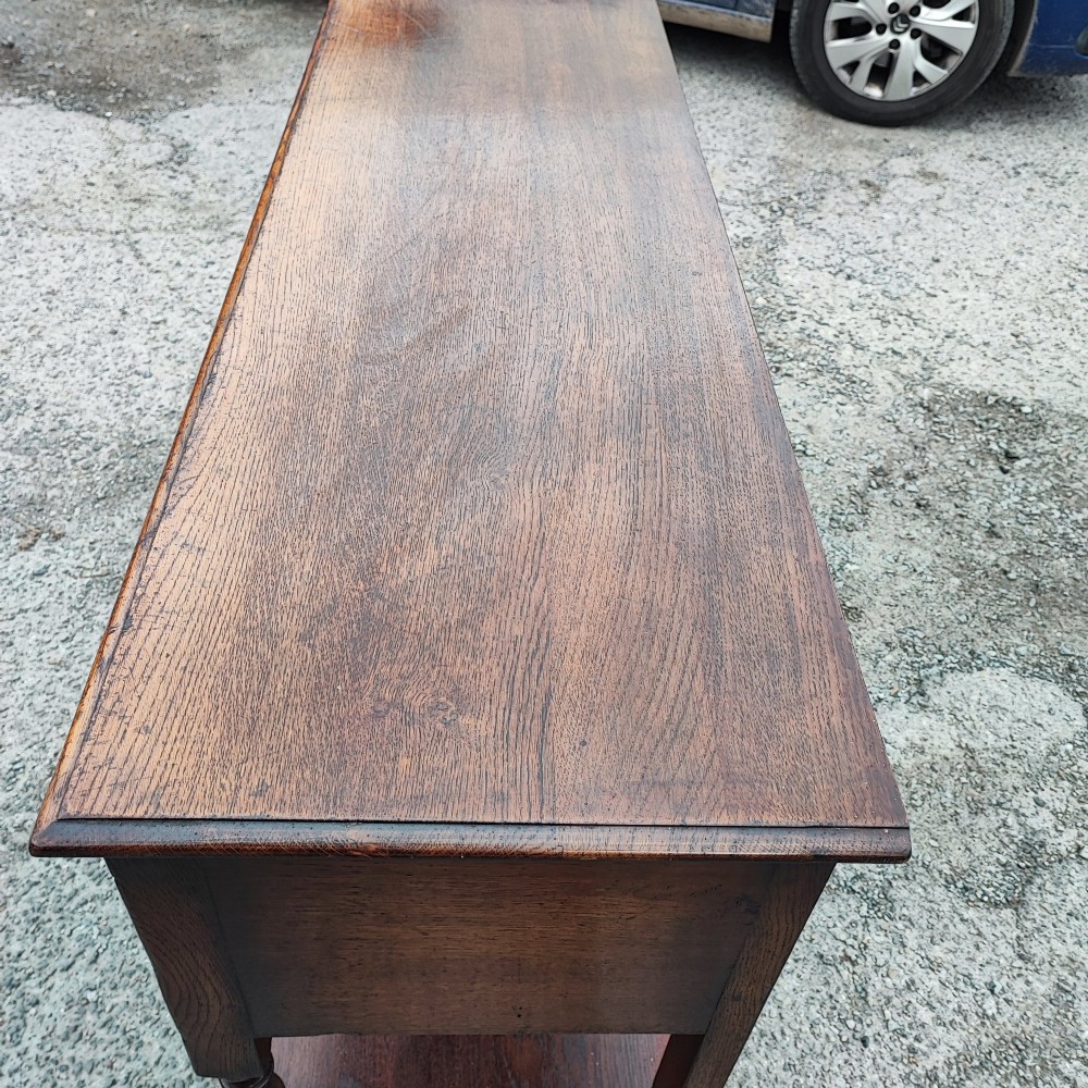 A low carved oak dresser base featuring geometric drawer mouldings, turned front legs, brass ring pulls, and an open lower pot shelf. View IV