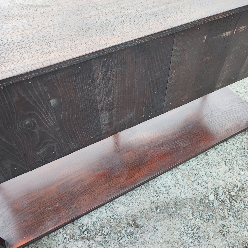A low carved oak dresser base featuring geometric drawer mouldings, turned front legs, brass ring pulls, and an open lower pot shelf. View V