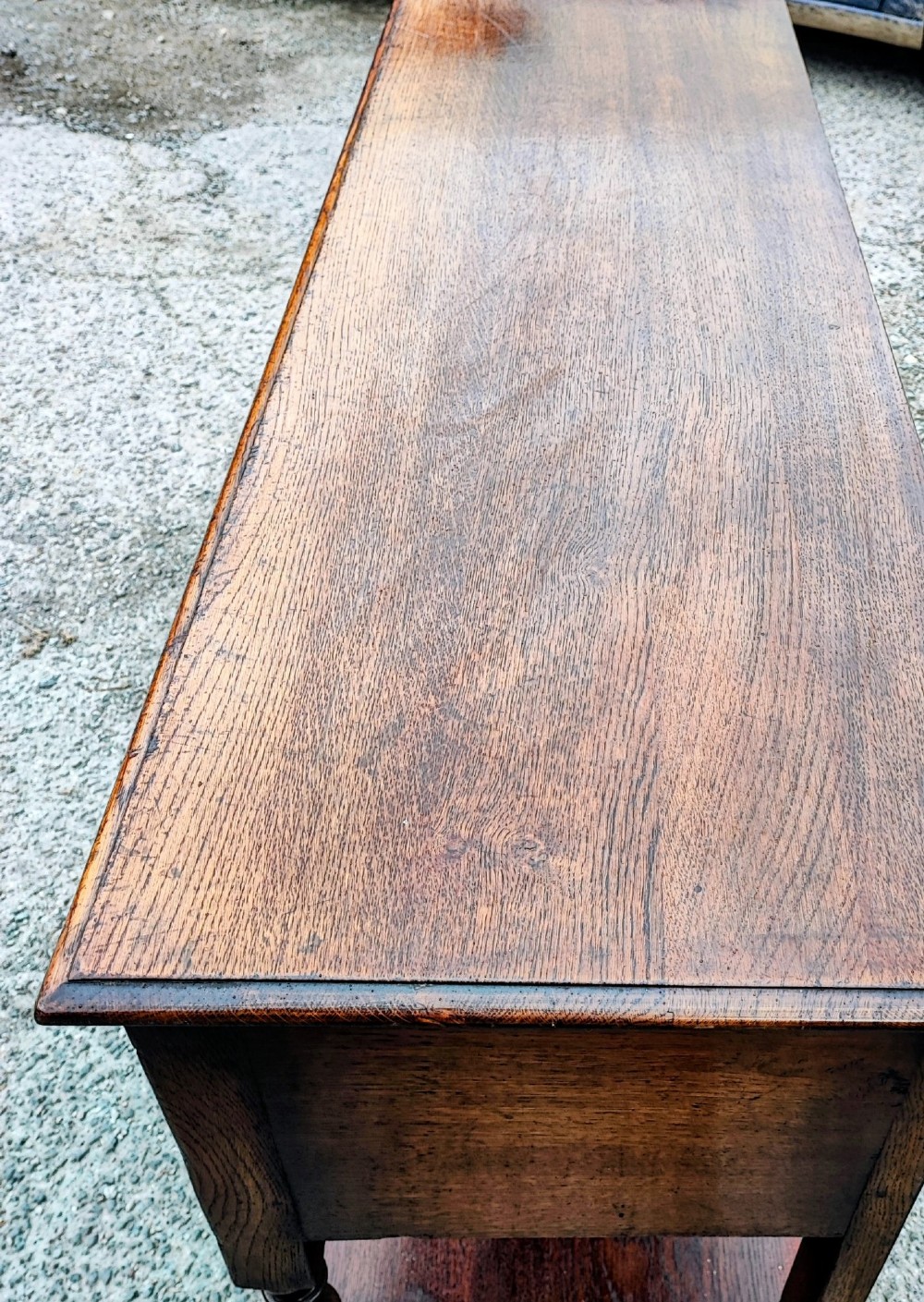 A low carved oak dresser base featuring geometric drawer mouldings, turned front legs, brass ring pulls, and an open lower pot shelf. View VI