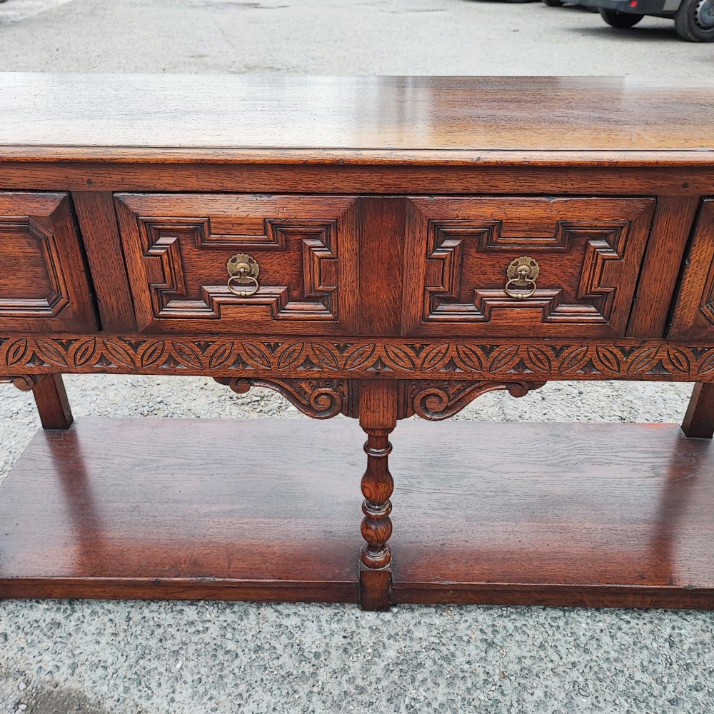A low carved oak dresser base featuring geometric drawer mouldings, turned front legs, brass ring pulls, and an open lower pot shelf. View VIII