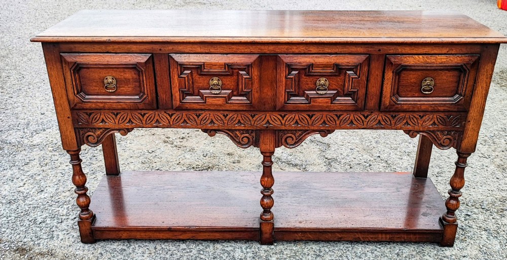 A low carved oak dresser base featuring geometric drawer mouldings, turned front legs, brass ring pulls, and an open lower pot shelf. View IX