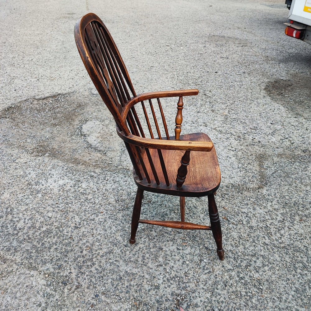 An antique dark brown wooden Windsor armchair featuring a steam-bent hoop back, a decorative pierced central splat, turned spindles, and a shaped elm seat. View III