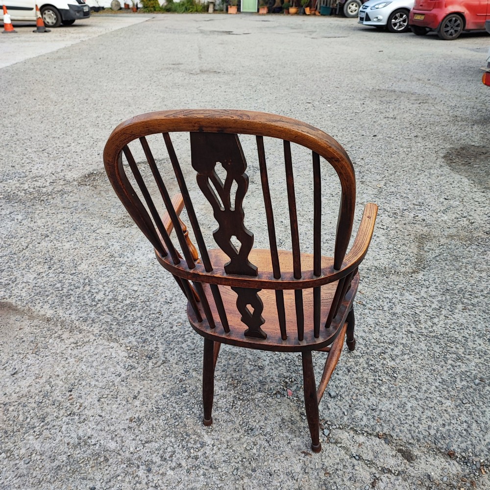 An antique dark brown wooden Windsor armchair featuring a steam-bent hoop back, a decorative pierced central splat, turned spindles, and a shaped elm seat. View IV