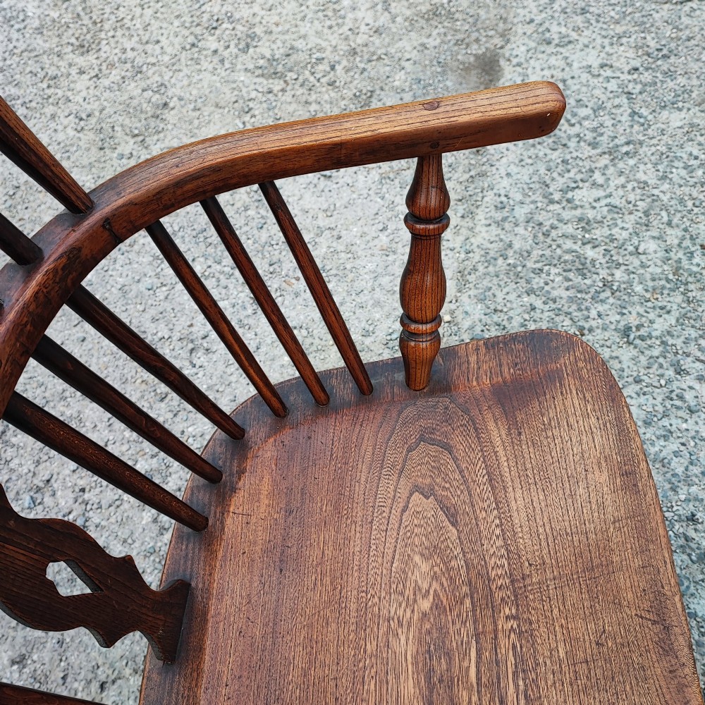 An antique dark brown wooden Windsor armchair featuring a steam-bent hoop back, a decorative pierced central splat, turned spindles, and a shaped elm seat. View V