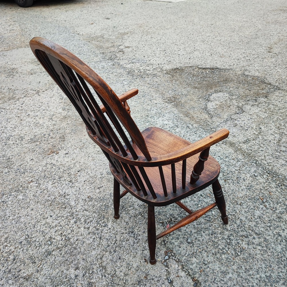 An antique dark brown wooden Windsor armchair featuring a steam-bent hoop back, a decorative pierced central splat, turned spindles, and a shaped elm seat. View VI