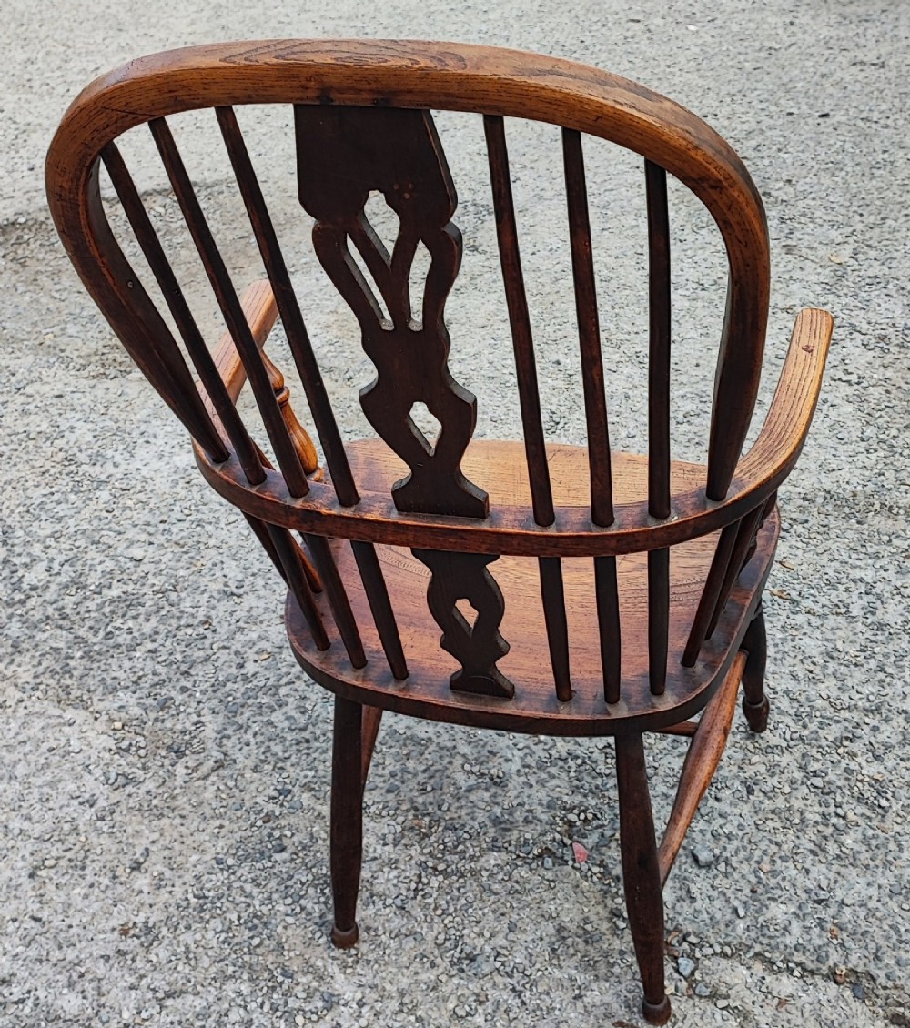 An antique dark brown wooden Windsor armchair featuring a steam-bent hoop back, a decorative pierced central splat, turned spindles, and a shaped elm seat. View VII
