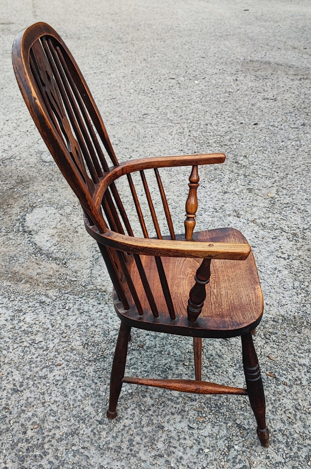 An antique dark brown wooden Windsor armchair featuring a steam-bent hoop back, a decorative pierced central splat, turned spindles, and a shaped elm seat. View VIII