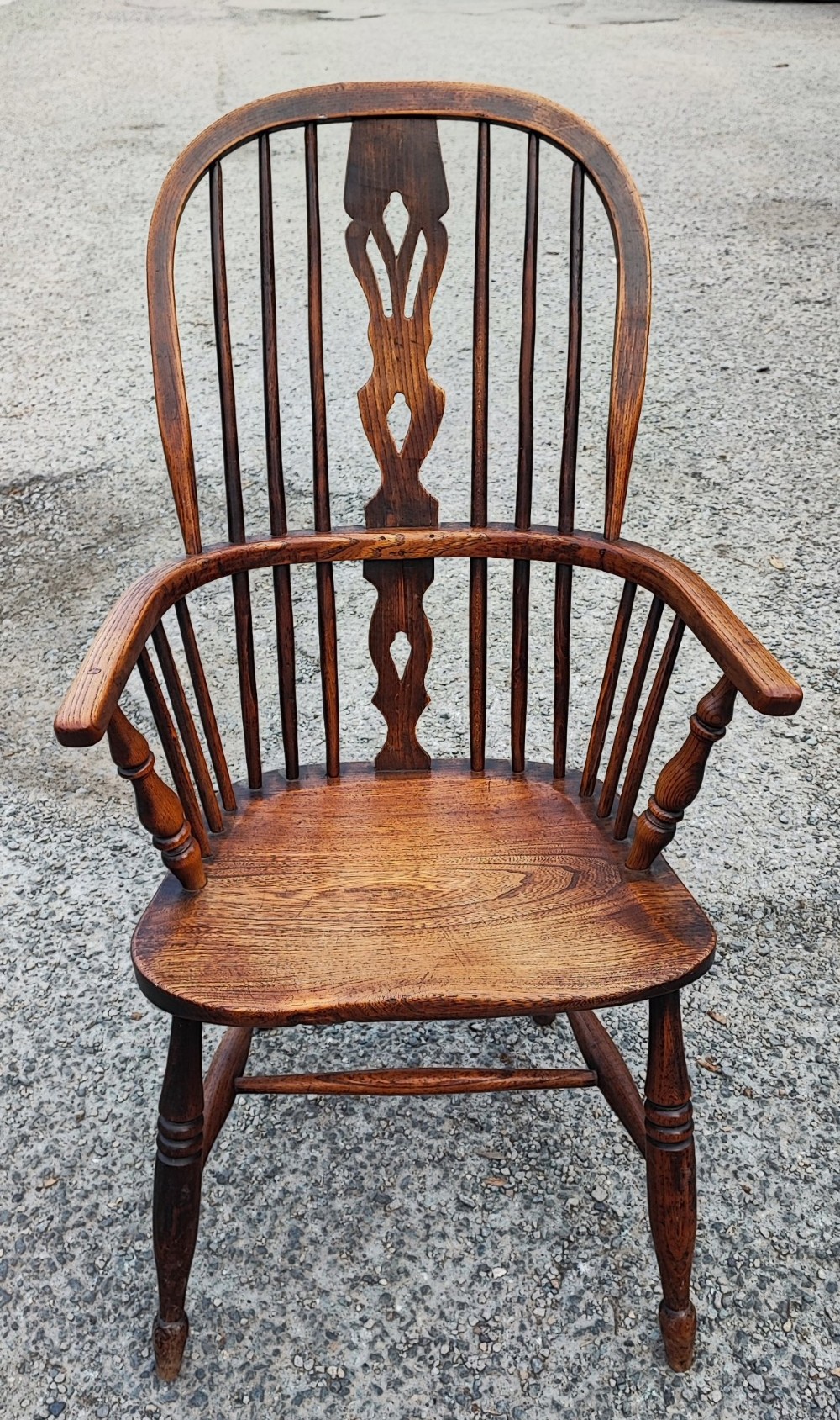 An antique dark brown wooden Windsor armchair featuring a steam-bent hoop back, a decorative pierced central splat, turned spindles, and a shaped elm seat. View IX