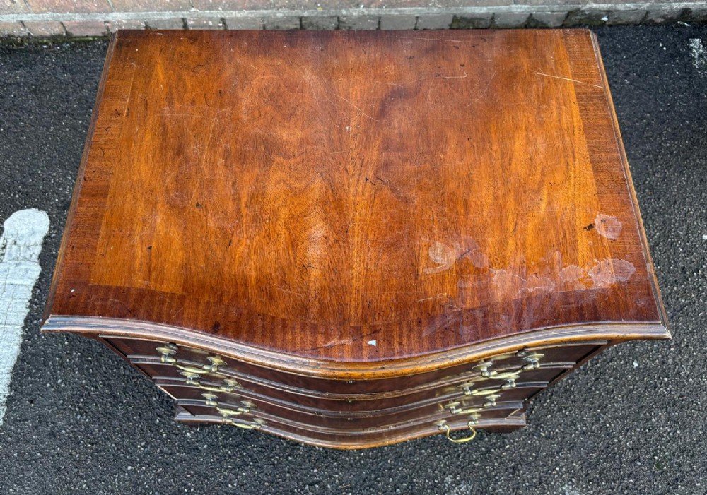 An antique mahogany chest of drawers featuring a serpentine front, four stacked drawers with brass handles, a pull-out brushing slide, and bracket feet. View II