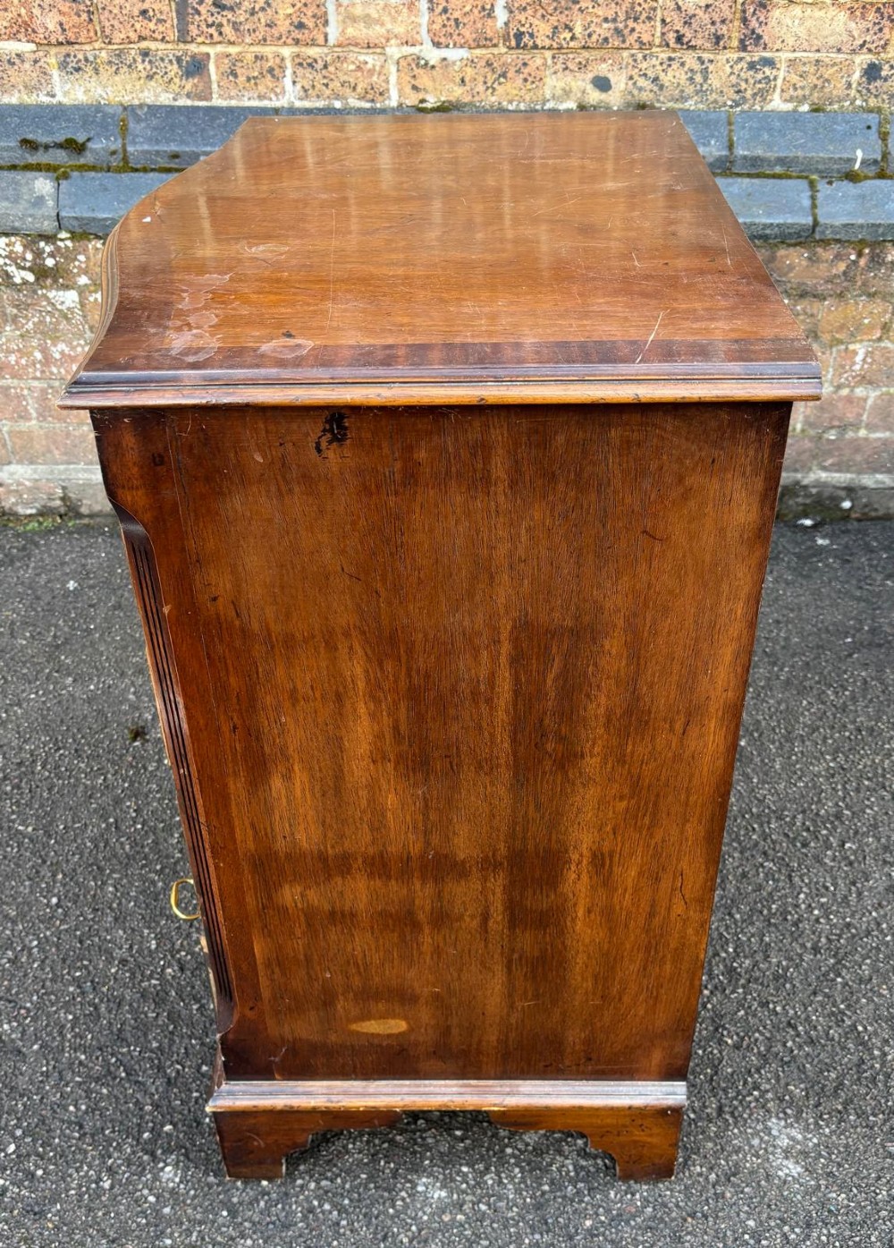 An antique mahogany chest of drawers featuring a serpentine front, four stacked drawers with brass handles, a pull-out brushing slide, and bracket feet. View III