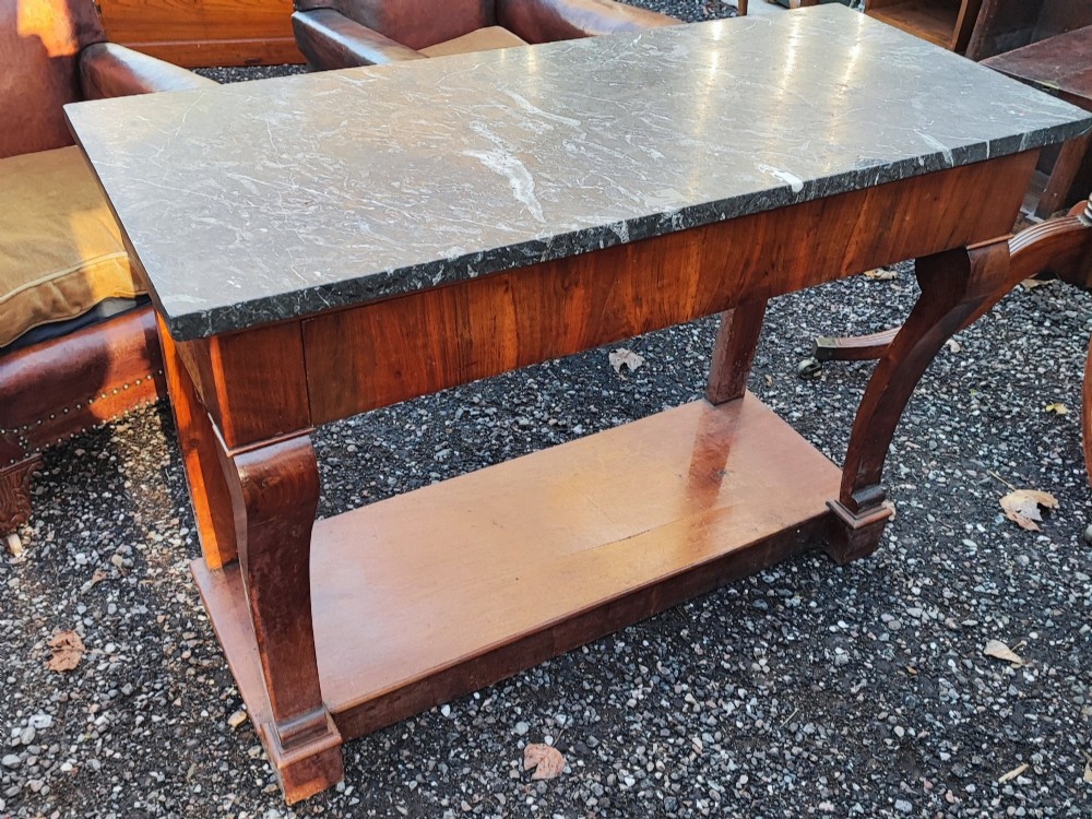 An antique French walnut console table featuring a thick grey veined marble top, scrolled front supports, and a lower plinth undertier.