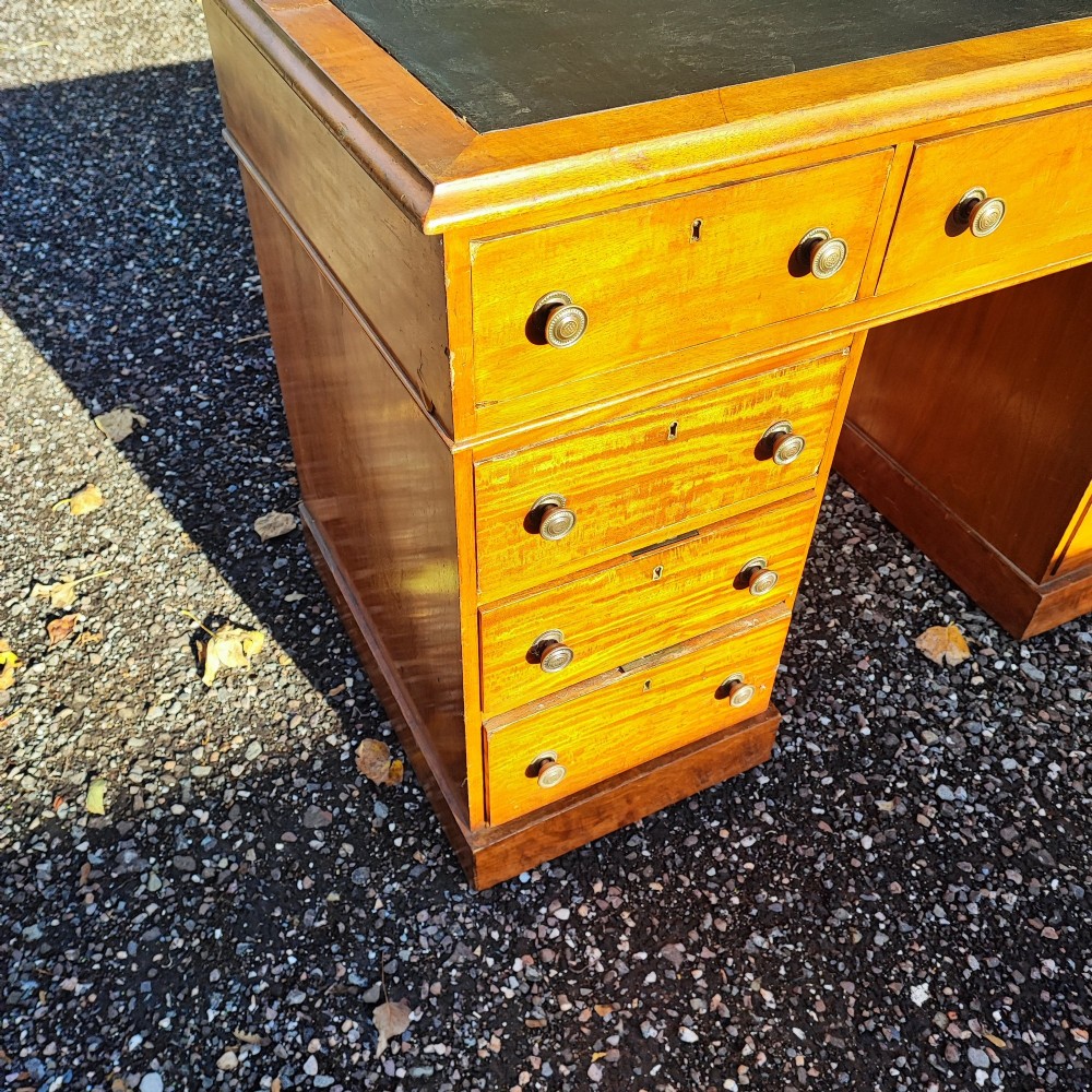 An antique blonde mahogany pedestal kneehole desk with a dark leather writing surface insert and nine drawers fitted with brass knob handles. View IV