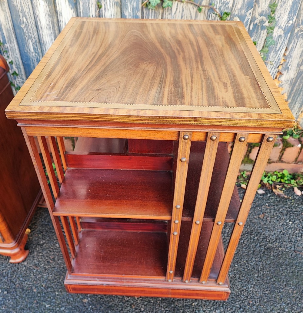 An Edwardian style square mahogany revolving bookcase featuring fine marquetry inlay along the top surface and vertical slatted sides accented with brass studs. View V
