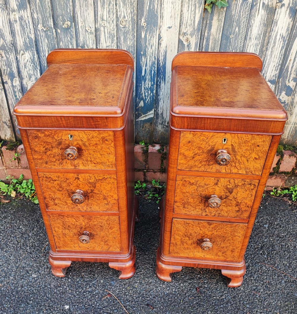 A pair of matching Art Deco burr walnut bedside cabinets featuring three drawers with carved wooden handles and a low raised gallery top.