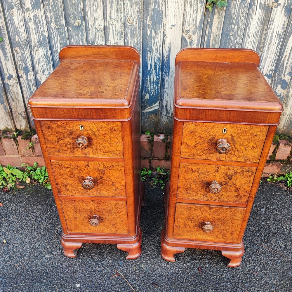 A pair of matching Art Deco burr walnut bedside cabinets featuring three drawers with carved wooden handles and a low raised gallery top. View II