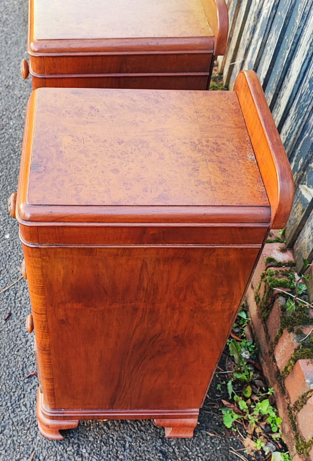 A pair of matching Art Deco burr walnut bedside cabinets featuring three drawers with carved wooden handles and a low raised gallery top. View IV