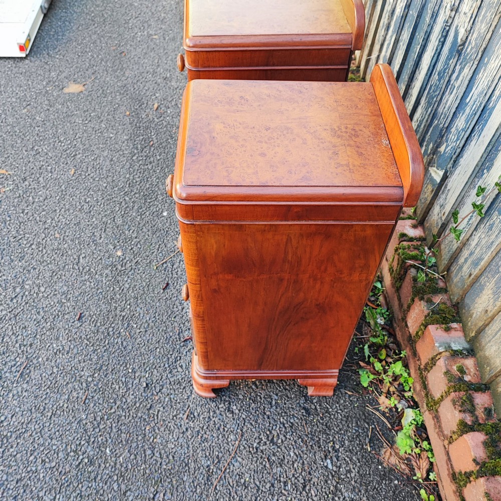 A pair of matching Art Deco burr walnut bedside cabinets featuring three drawers with carved wooden handles and a low raised gallery top. View V
